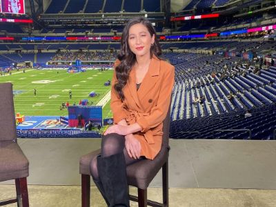 Mina Kimes is sitting in a chair with her legs crossed in a stadium.